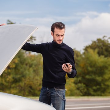 carchex features extended car warranty provider car broke down man in black sweater holds phone and open hood 